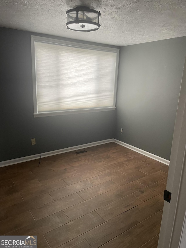 unfurnished room with a textured ceiling, dark wood-style flooring, visible vents, and baseboards