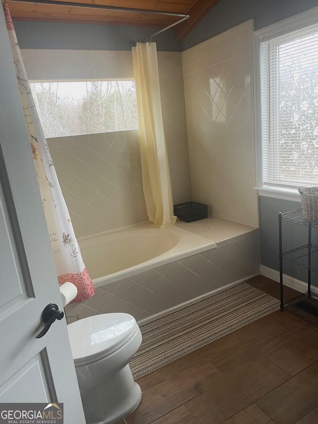 bathroom featuring baseboards, tiled shower / bath, toilet, and wood finished floors