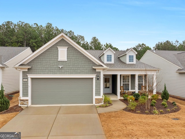 view of front facade featuring driveway, covered porch, an attached garage, and roof with shingles