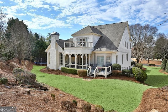 rear view of house featuring a lawn, a trampoline, and a balcony