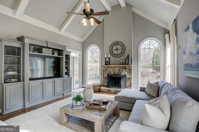 living area with a wealth of natural light, beam ceiling, a stone fireplace, and wood finished floors