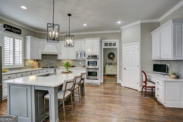 kitchen with a breakfast bar, custom exhaust hood, appliances with stainless steel finishes, built in study area, and a sink