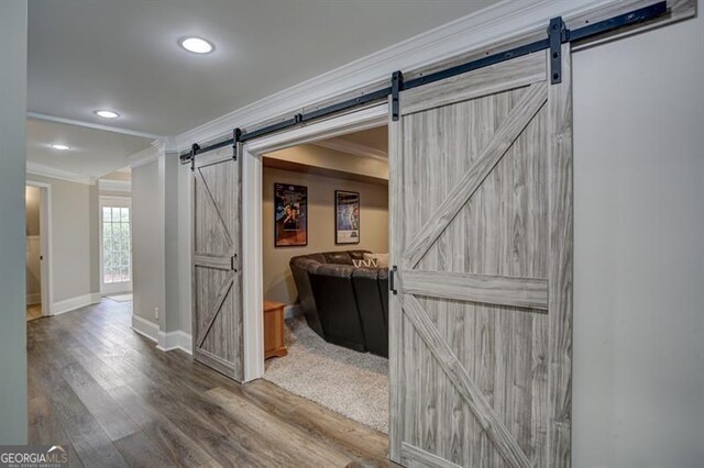 hallway with a barn door, baseboards, wood finished floors, crown molding, and recessed lighting