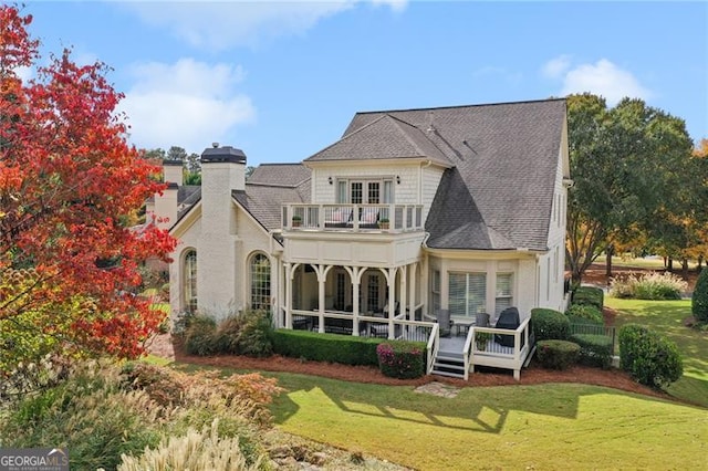 rear view of property featuring a shingled roof, a lawn, a chimney, and a balcony