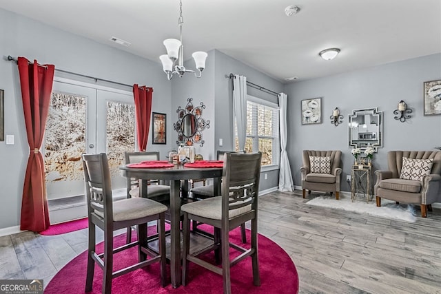 dining area featuring baseboards, visible vents, wood finished floors, french doors, and a notable chandelier