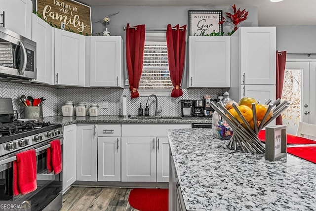 kitchen with stainless steel appliances, wood finished floors, a sink, light stone countertops, and tasteful backsplash