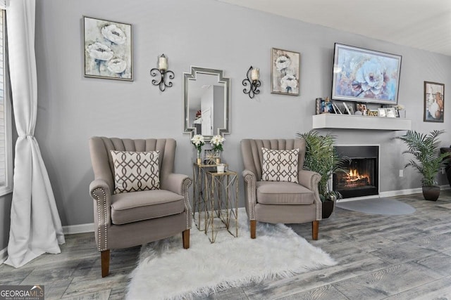 living area featuring a fireplace with flush hearth, wood finished floors, and baseboards