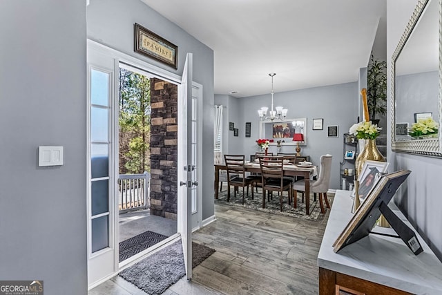 doorway to outside with a notable chandelier and wood finished floors