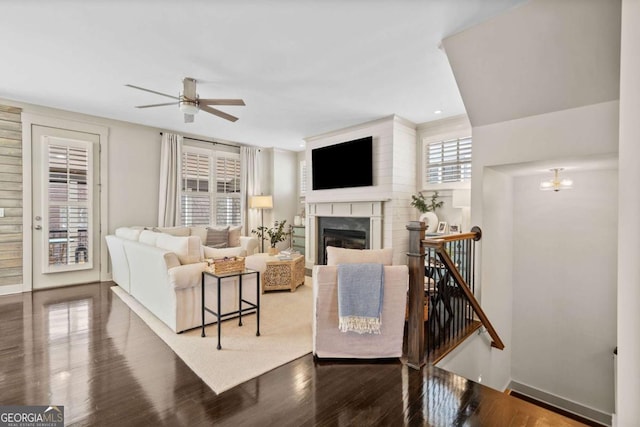 living area featuring a ceiling fan, a glass covered fireplace, baseboards, and wood finished floors