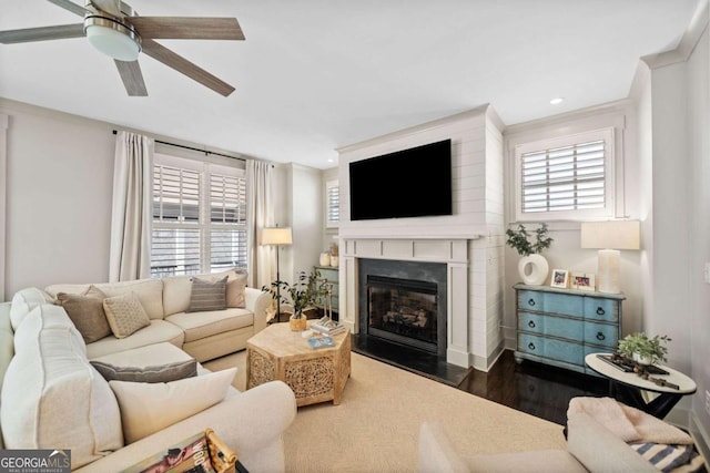 living room featuring a glass covered fireplace, dark wood-style floors, ceiling fan, crown molding, and recessed lighting