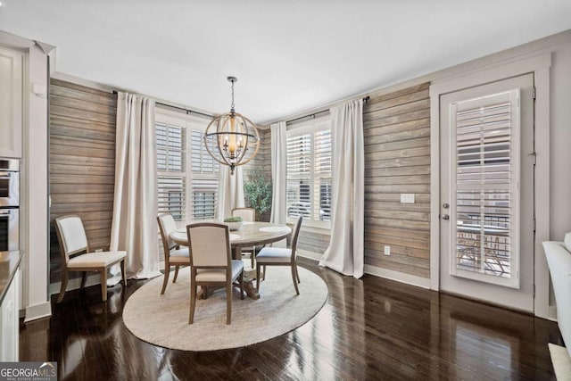 dining room featuring a chandelier, baseboards, dark wood finished floors, and wooden walls