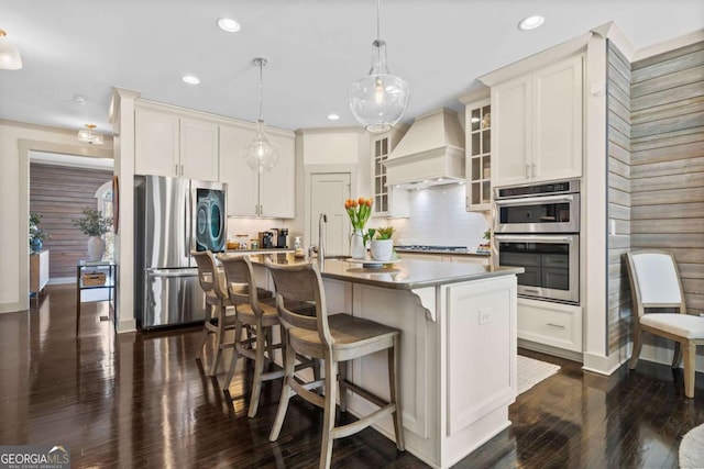 kitchen featuring a center island with sink, dark wood finished floors, appliances with stainless steel finishes, custom exhaust hood, and a sink