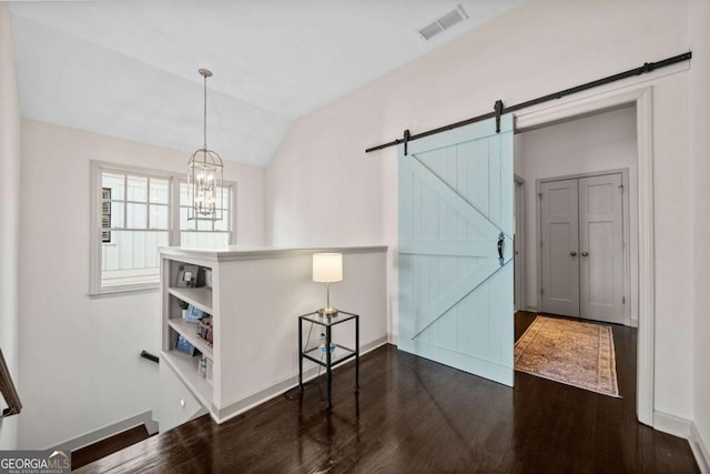 dining room featuring a barn door, wood finished floors, visible vents, baseboards, and vaulted ceiling