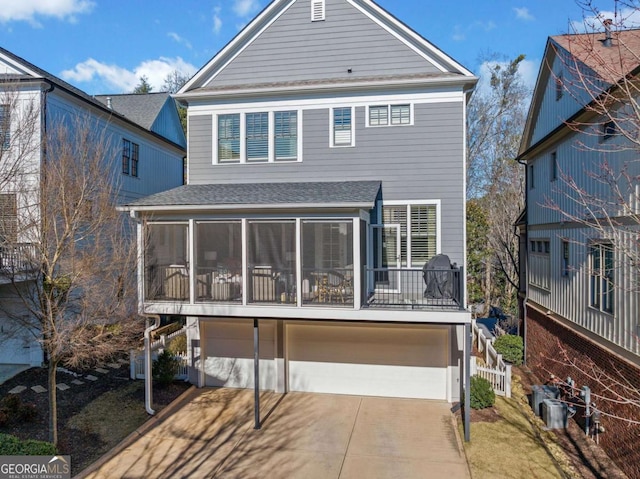 back of property featuring a garage, driveway, a shingled roof, and a sunroom