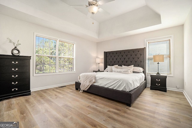 bedroom featuring light wood finished floors, visible vents, baseboards, and a raised ceiling