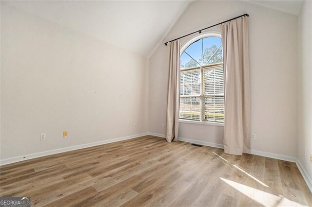 spare room with vaulted ceiling, a wealth of natural light, and wood finished floors