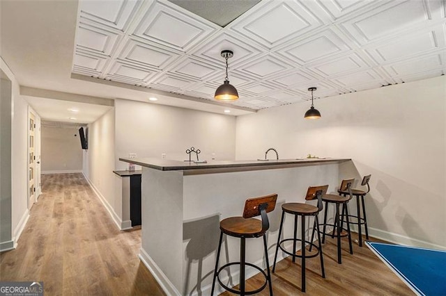 kitchen with an ornate ceiling, a breakfast bar area, wood finished floors, a peninsula, and baseboards