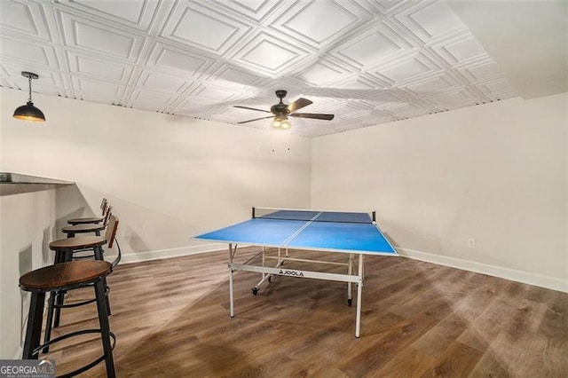 recreation room with a ceiling fan, wood finished floors, an ornate ceiling, and baseboards