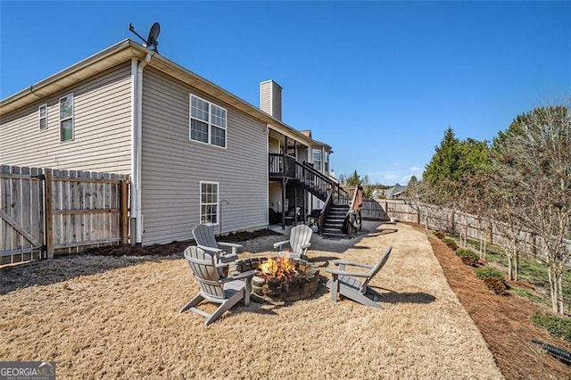 rear view of property with a fenced backyard, stairs, a fire pit, and a chimney