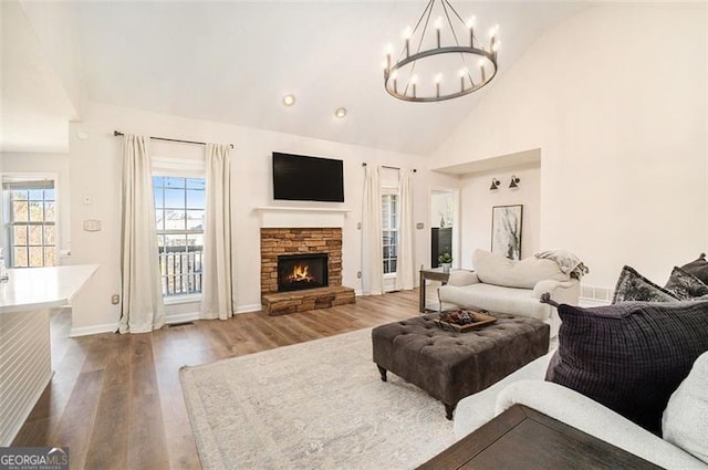 living area with baseboards, wood finished floors, a stone fireplace, high vaulted ceiling, and a notable chandelier