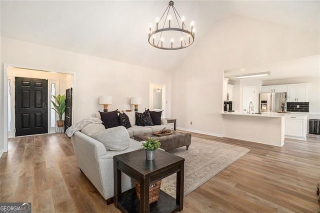 living room with baseboards, high vaulted ceiling, light wood-type flooring, and a notable chandelier