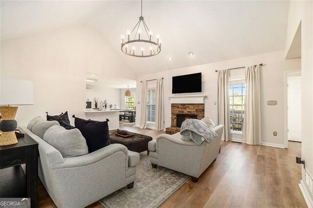 living area with high vaulted ceiling, a stone fireplace, a chandelier, light wood-type flooring, and baseboards