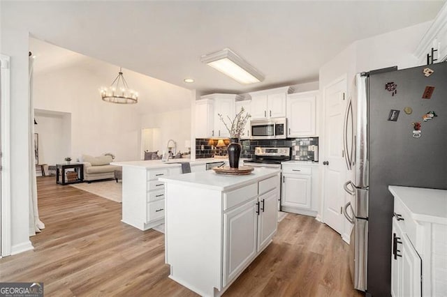 kitchen with light wood finished floors, a peninsula, stainless steel appliances, white cabinetry, and backsplash