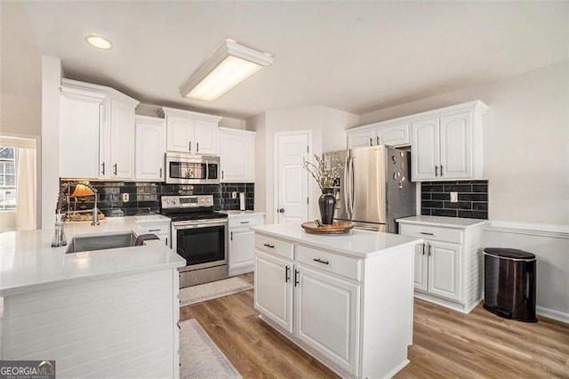 kitchen with light wood finished floors, white cabinets, appliances with stainless steel finishes, light countertops, and a sink