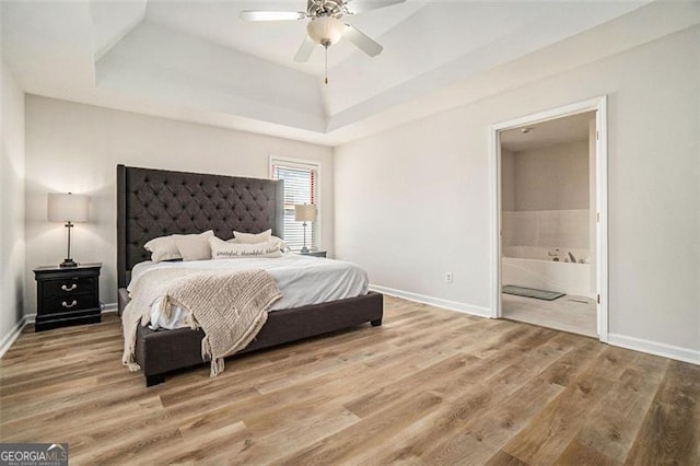 bedroom featuring a raised ceiling, connected bathroom, baseboards, and wood finished floors