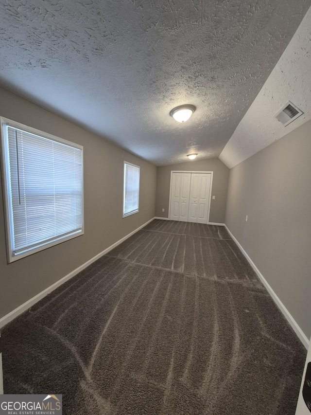 unfurnished bedroom featuring carpet, a textured ceiling, vaulted ceiling, visible vents, and baseboards