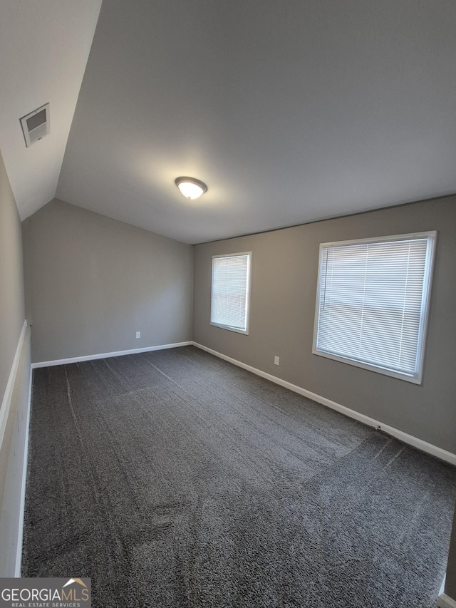 unfurnished room featuring baseboards, dark colored carpet, and vaulted ceiling