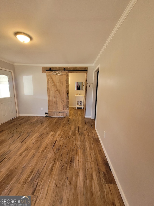 interior space featuring a barn door, crown molding, baseboards, and wood finished floors