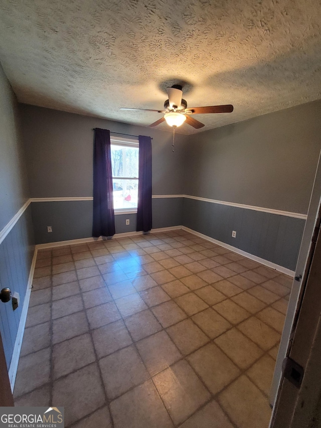 spare room with a wainscoted wall, ceiling fan, and a textured ceiling