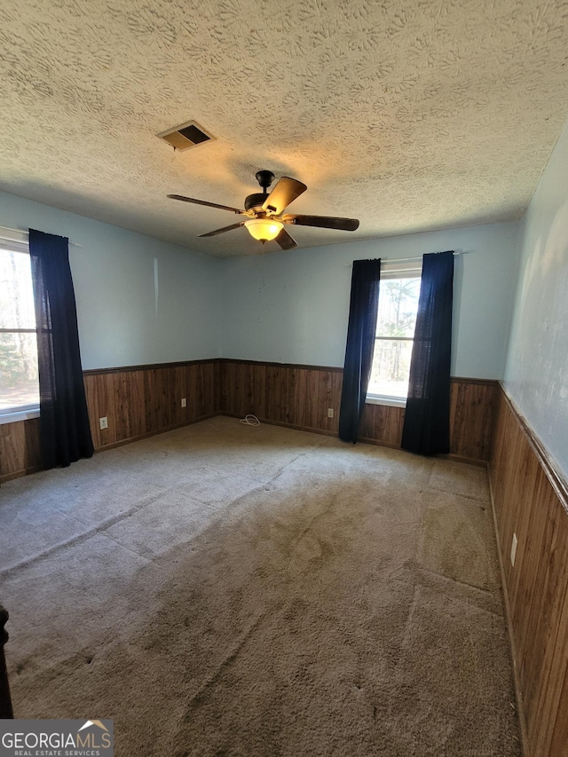 spare room with carpet, visible vents, wainscoting, wooden walls, and a textured ceiling