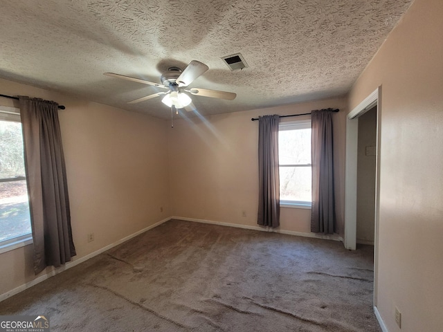 carpeted empty room with ceiling fan, visible vents, baseboards, and a textured ceiling