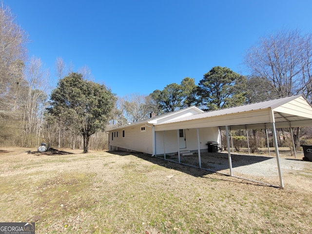 back of property with driveway, a detached carport, and a yard