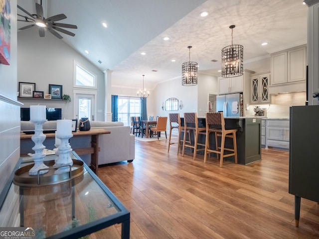 living room with light wood-style flooring, ceiling fan with notable chandelier, crown molding, high vaulted ceiling, and recessed lighting