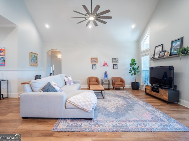 living area featuring arched walkways, high vaulted ceiling, ceiling fan, wood finished floors, and baseboards