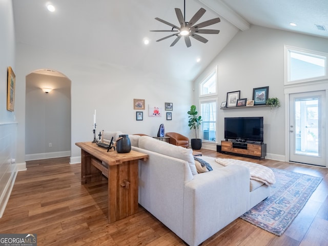 living room featuring high vaulted ceiling, arched walkways, beamed ceiling, and wood finished floors