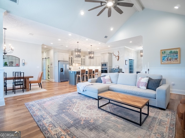 living area featuring high vaulted ceiling, light wood-style flooring, ceiling fan with notable chandelier, visible vents, and beam ceiling