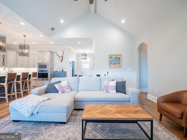 living room featuring arched walkways, beam ceiling, light wood-type flooring, and visible vents