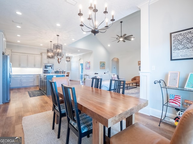 dining area with arched walkways, high vaulted ceiling, ceiling fan with notable chandelier, ornamental molding, and light wood finished floors