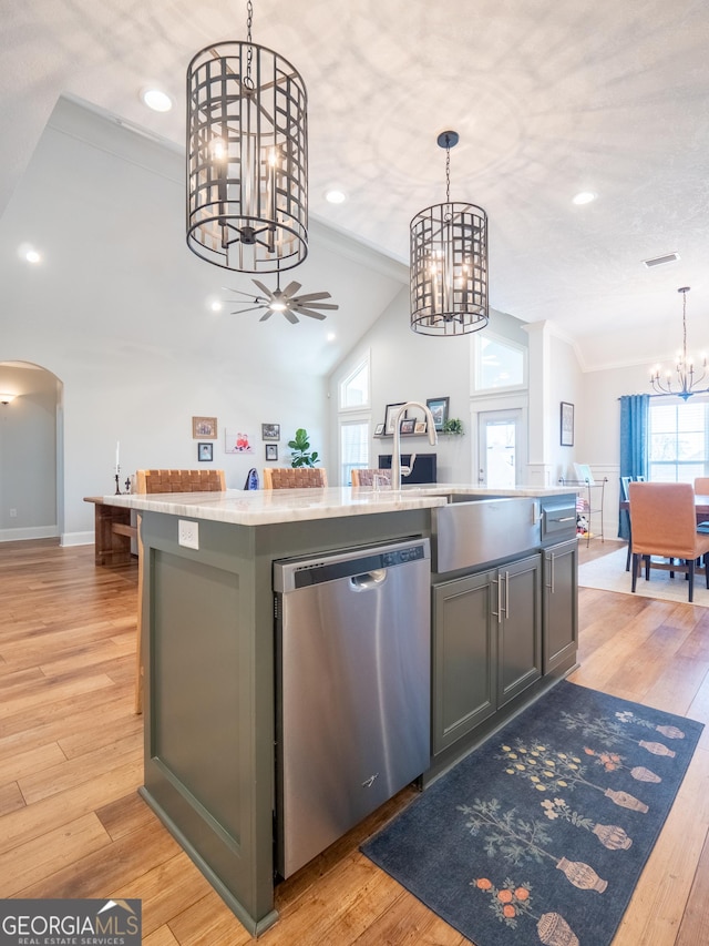 kitchen featuring arched walkways, light wood-style flooring, vaulted ceiling, stainless steel dishwasher, and a center island with sink