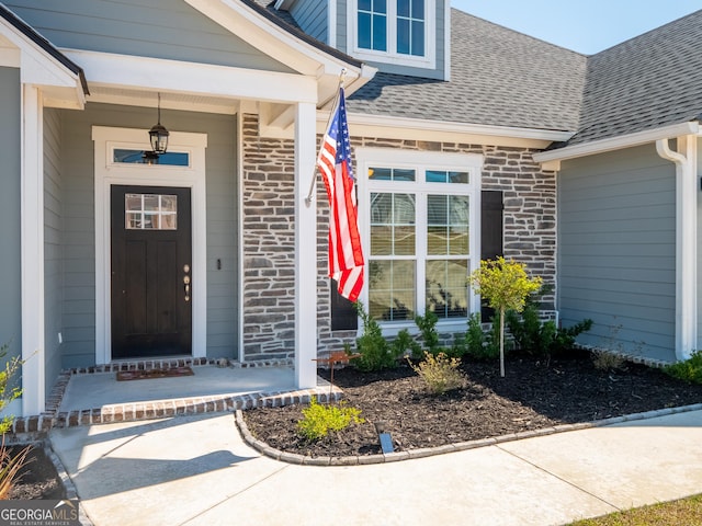 property entrance with stone siding, covered porch, roof with shingles, and brick siding