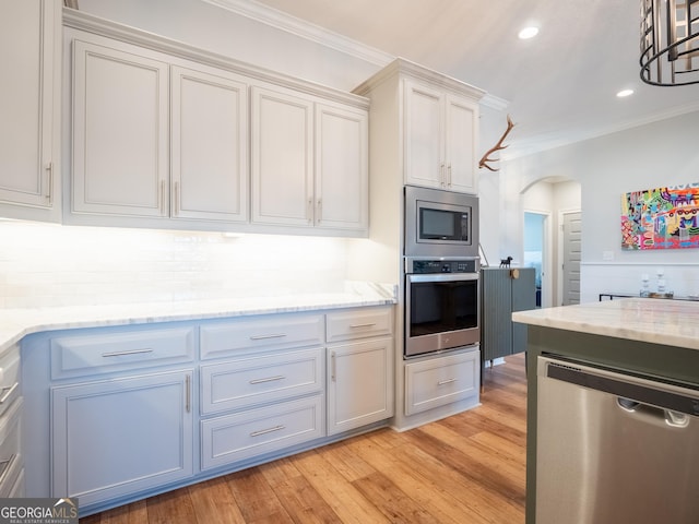 kitchen with arched walkways, light stone counters, appliances with stainless steel finishes, light wood finished floors, and crown molding