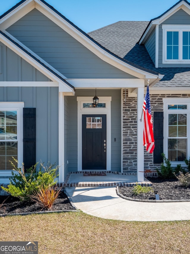 property entrance with board and batten siding, roof with shingles, and brick siding