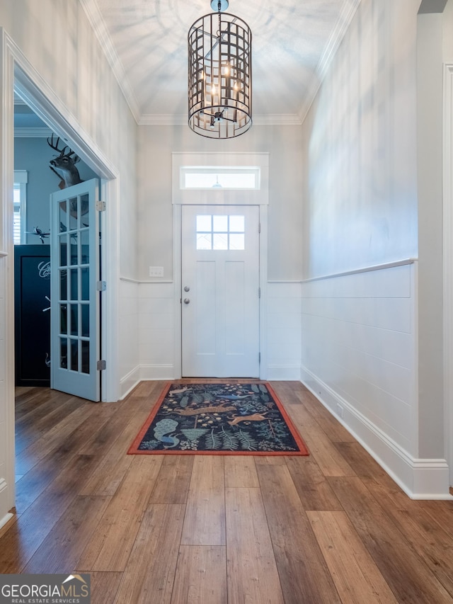 entryway featuring a notable chandelier, hardwood / wood-style floors, wainscoting, and crown molding