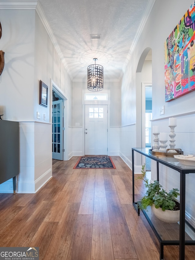 foyer with arched walkways, a textured ceiling, hardwood / wood-style flooring, wainscoting, and crown molding