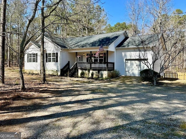 view of front of property featuring a shingled roof, covered porch, an attached garage, and gravel driveway