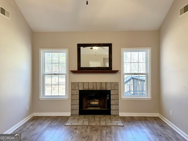 unfurnished living room featuring a brick fireplace, visible vents, and wood finished floors